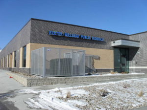 A perforated metal fence surrounding a heating and cooling unit in front of a school