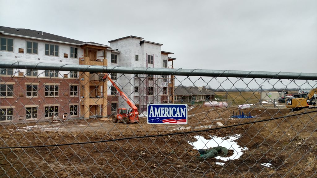 The American Fence nameplate on a temporary fence panel with the under-construction retirement home in the background