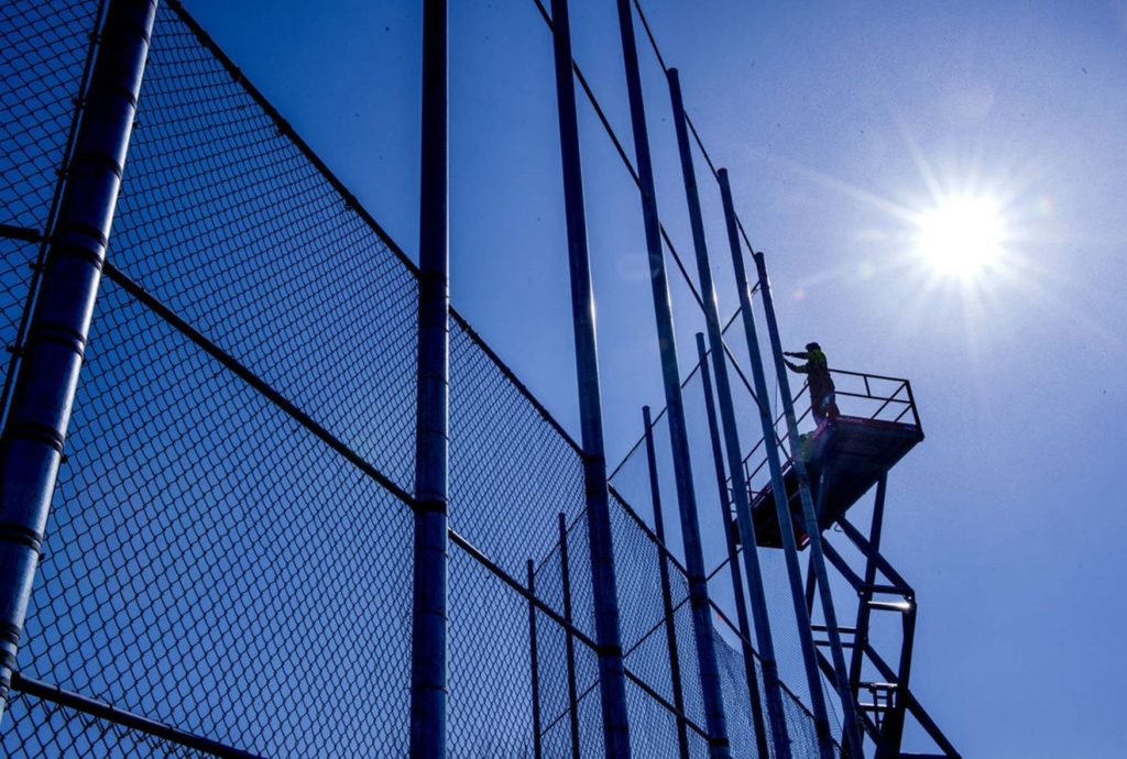 An American Fence Company worker on a lift installing chain link fabric on a 40-foot backstop