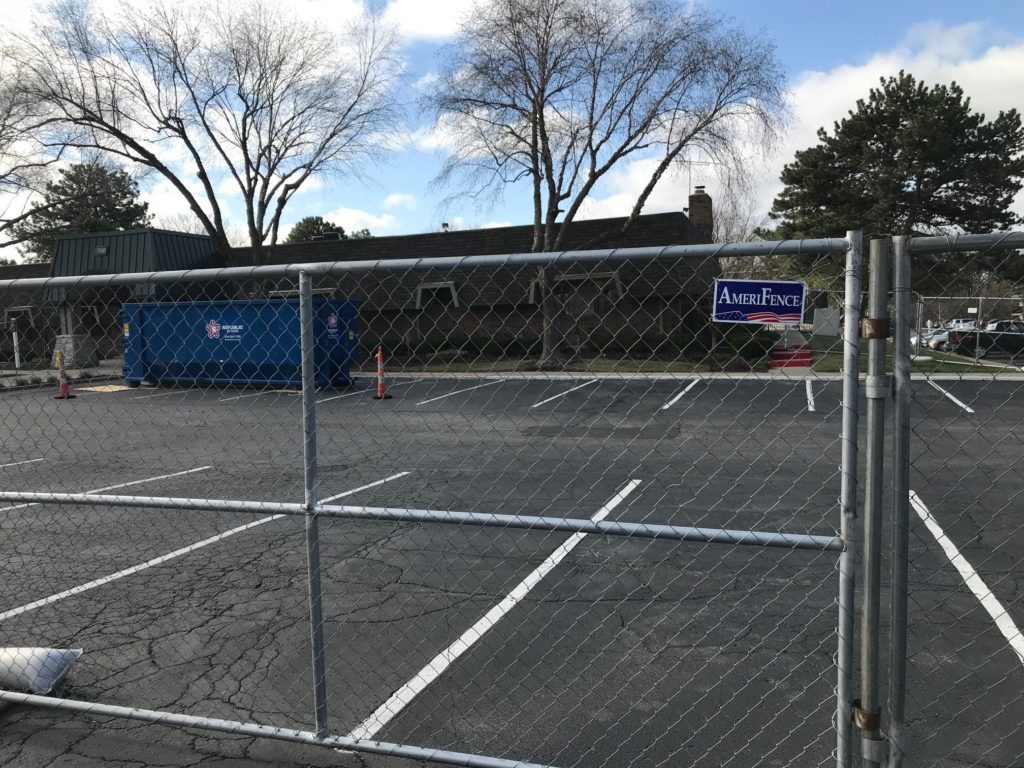 Chain link temp fence surrounding an asphalt parking lot with an "AmeriFence" name plate attached to the mesh