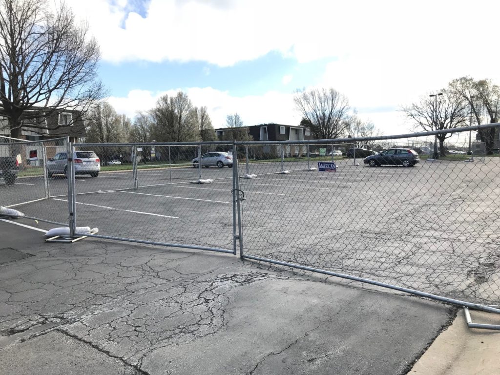 Temporary construction fencing around an asphalt parking lot with a double swing gate wide enough to allow cars and construction vehicles